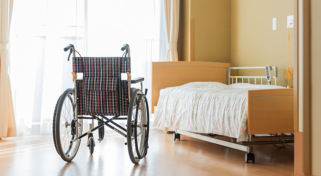 Empty bed and empty wheelchair in room of a nursing home.